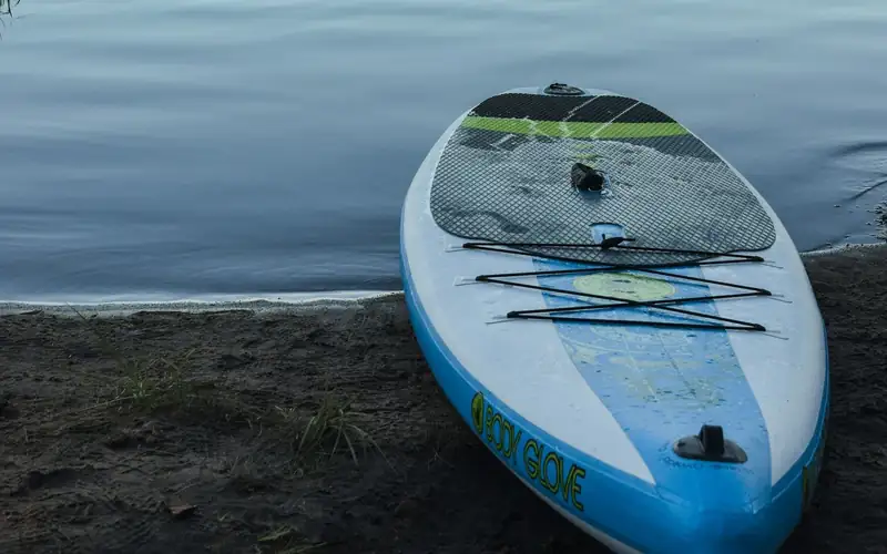 Opgeblazen blauw-wit SUP board ligt op de oever van een meer