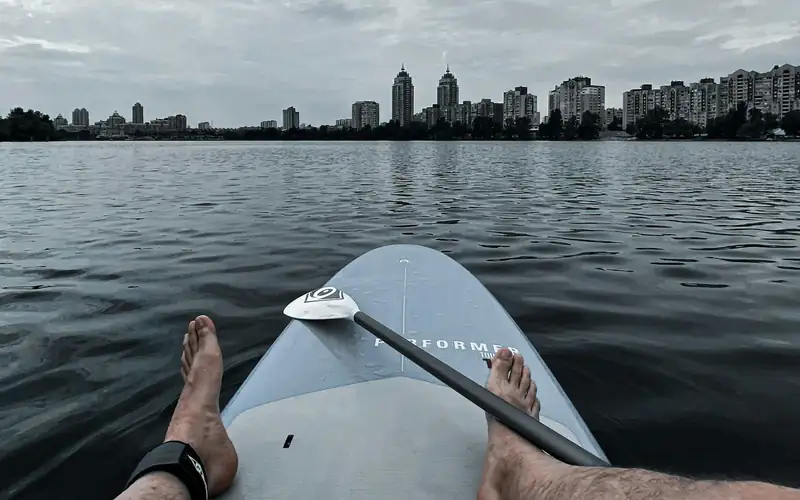 Uitzicht vanaf een SUP board met blote voeten op een grijs, rimpelend water onder zware bewolking